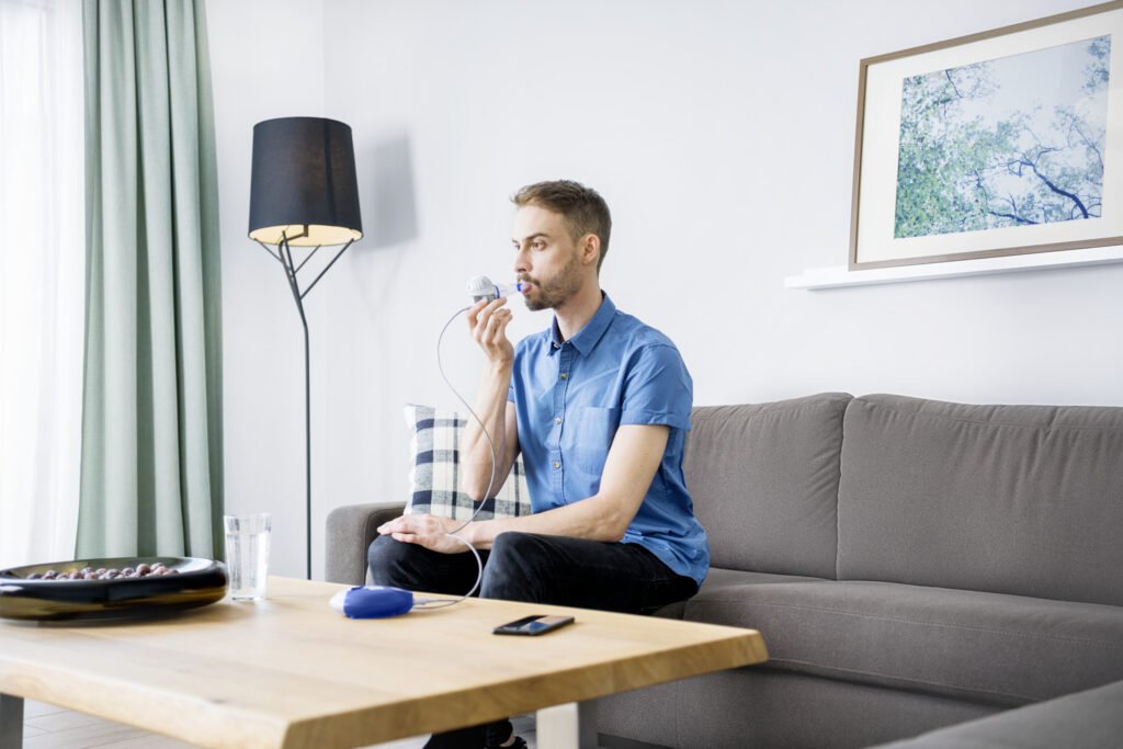 El hombre inhala con un sistema de inhalación mientras está sentado en el sofá.